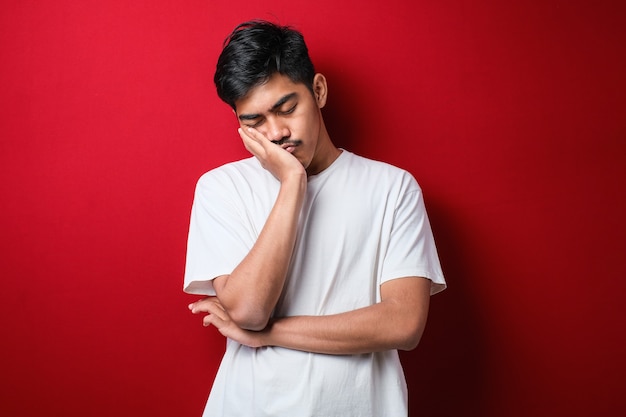 Young asian man wearing white t-shirt over red background thinking looking tired and bored with depression problems with crossed arms