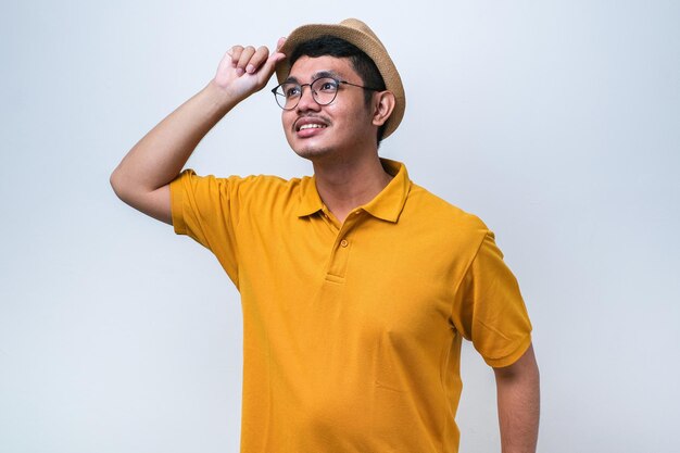 Young asian man wearing white tshirt looks very happy and smiling looking far away with hand over head over white background searching concept