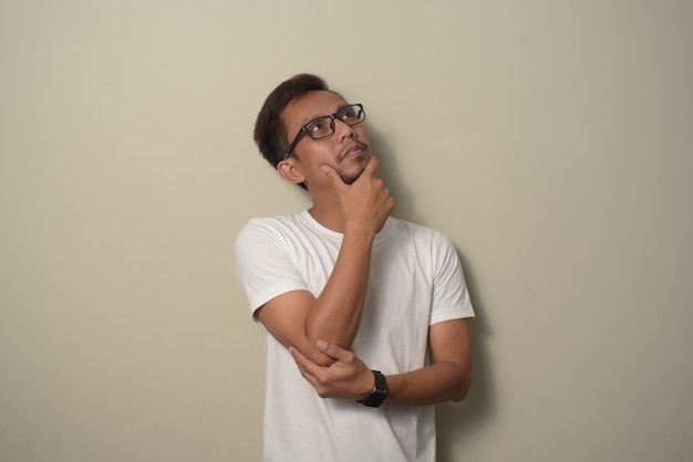 Young Asian man wearing white tshirt with hand on chin thinking about question pensive expression