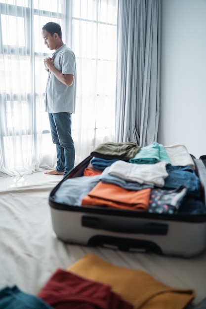 Young Asian man wears a shirt after opening his suitcase in the bedroom