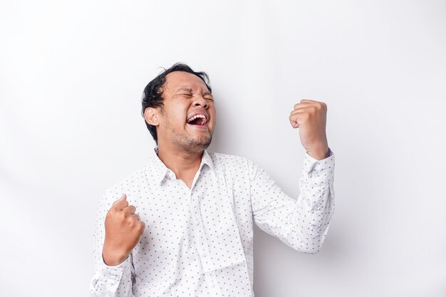 A young Asian man with a happy successful expression wearing white shirt isolated by white background