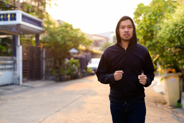 Young Asian man with hoodie jogging in the streets outdoors