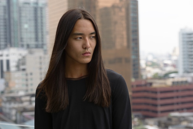 야외에서 도시에서 생각하는 긴 머리를 가진 젊은 아시아 남자