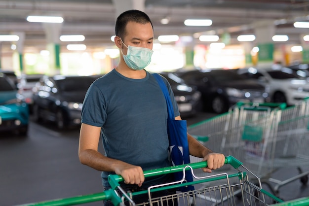 駐車場でショッピングカートを保持しているマスクを持つ若いアジア男