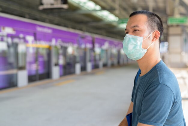 코로나 바이러스 발발 대기 및 스카이 트레인 역에 앉아 보호 마스크를 가진 젊은 아시아 남자