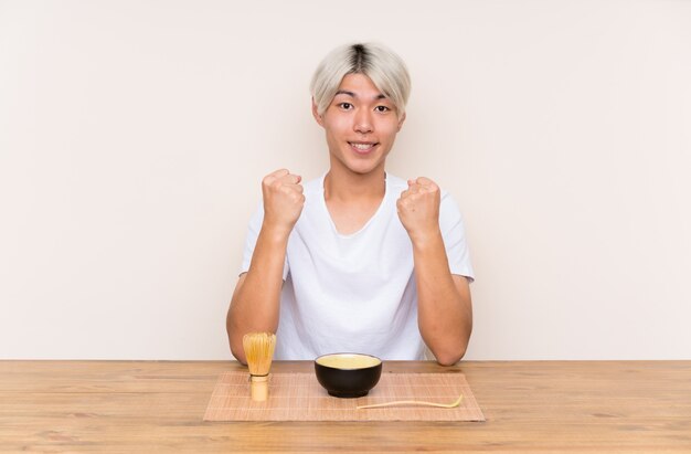 Young asian man with matcha tea in a table celebrating a victory