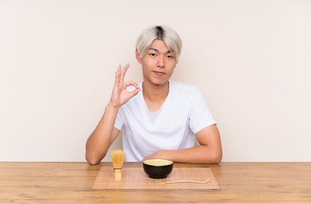 Young asian man with matcha tea in a table showing an ok sign with fingers