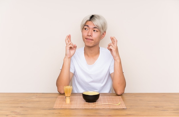 Young asian man with matcha tea in a table with fingers crossing