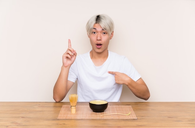 Молодой азиатский человек с чаем матча в таблице с выражением лица сюрприза