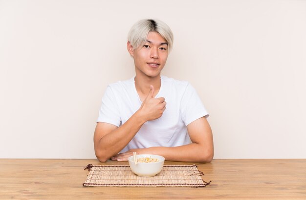 Young asian man with ramen in a table giving a thumbs up gesture