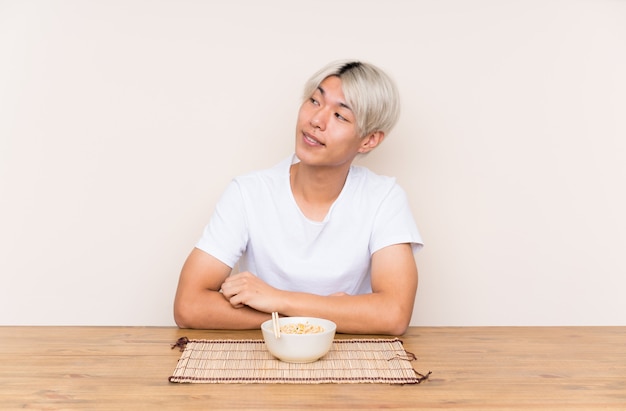 Young asian man with ramen in a table laughing and looking up