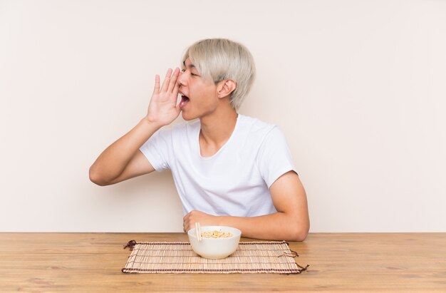 口を大きく開けて叫んでテーブルにラーメンを持つ若いアジア人