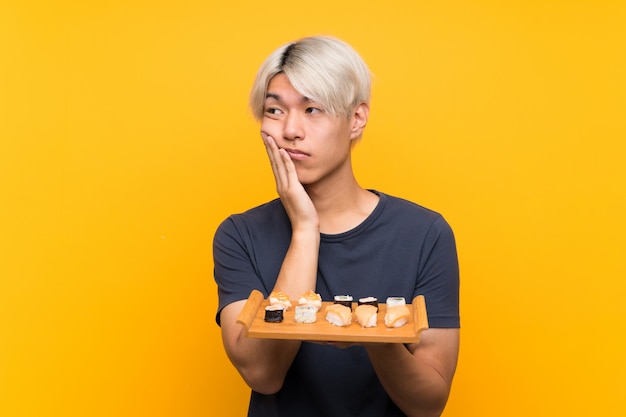 Young asian man with sushi over isolated yellow unhappy and frustrated