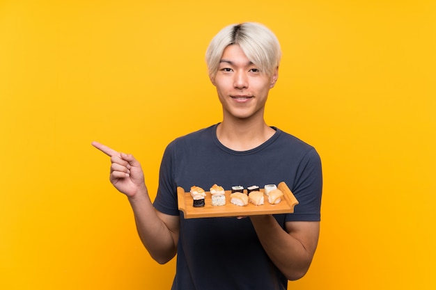 Young asian man with sushi  pointing finger to the side