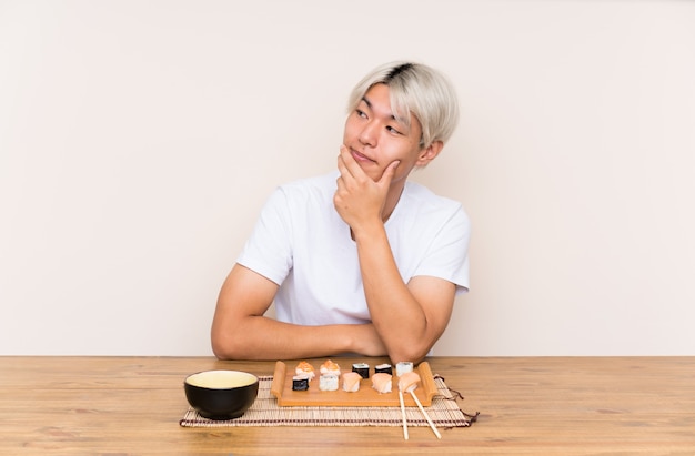 Young asian man with sushi in a table thinking an idea