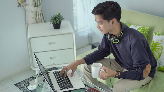 Young asian man working from home using his laptop with a cup of drink