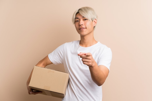 Young asian manholding a box to move it to another site while pointing to the front