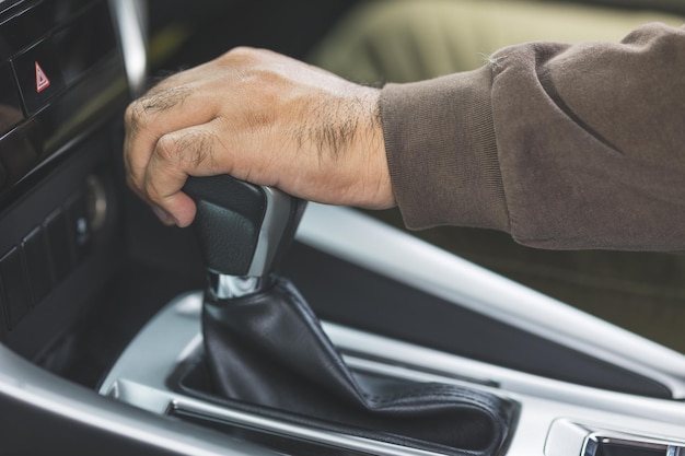 新しい車を手に入れる若いアジア人男性と彼の手は、高級車のスティックシフトトランスミッションを制御します。車を運転する男性の手がギアを変更します。