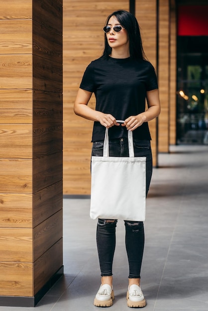 Young asian model girl dressed in a sunglasses on the street\
holding white eco bag mock up