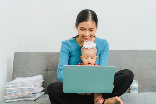 Young Asian mom with cute baby daughter sitting at sofa together in the living room