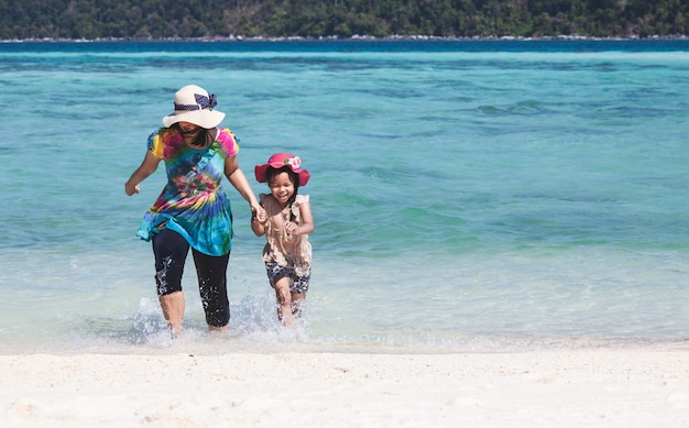 若いアジアの母親とかわいい小さな娘が美しい海で一緒に水を遊ぶ