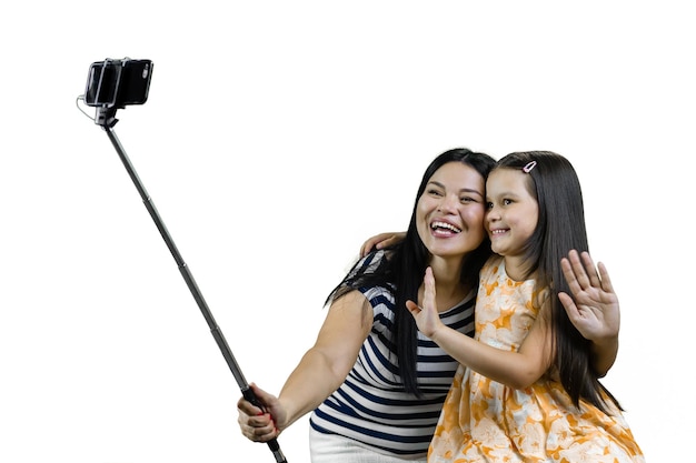 写真 アジアの若い母親と娘が、白い背景に隔離された自撮り棒を使ってスマートフォンで自撮りをする