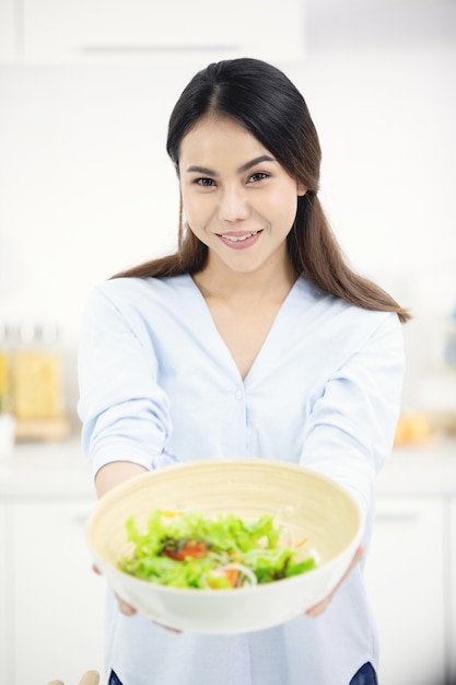 Giovane madre asiatica che produce cibo in cucina con la faccia di sorriso.
