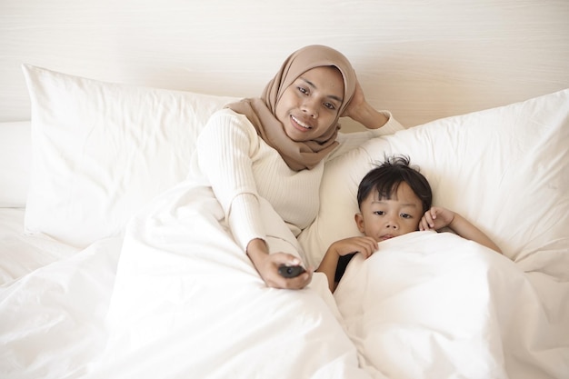 Young asian mother playing on bed happily in hotel room on vacation