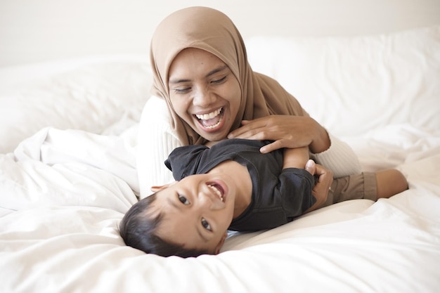 Young asian mother and son playing on bed cheerfully in hotel room on vacation