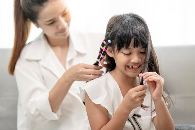 Young Asian mother tying daughter's hair