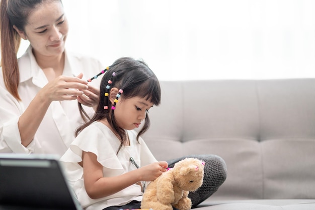 娘の髪を結ぶ若いアジア人の母親