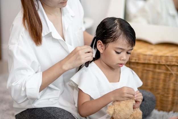 娘の髪を結ぶ若いアジア人の母親