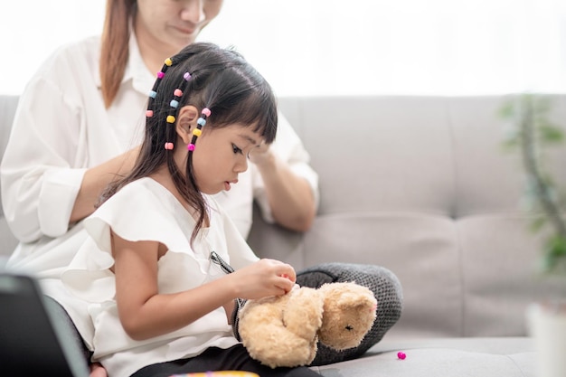 Молодая азиатская мать завязывает волосы дочери