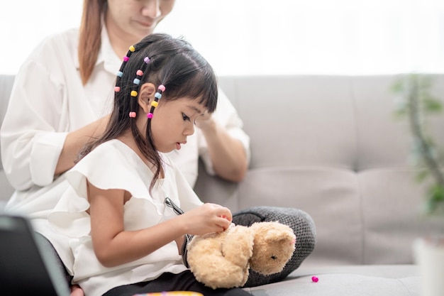 Young Asian mother tying daughter's hair