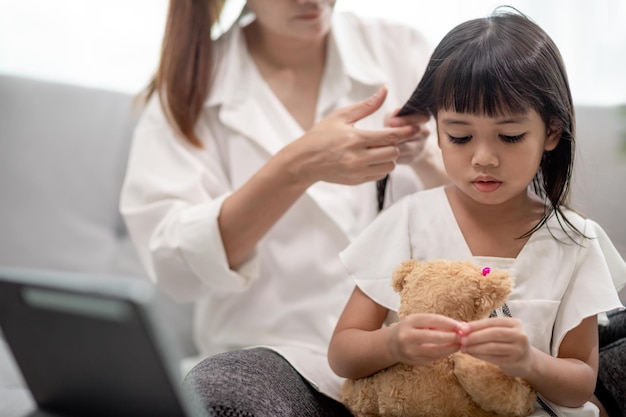 Young Asian mother tying daughter's hair