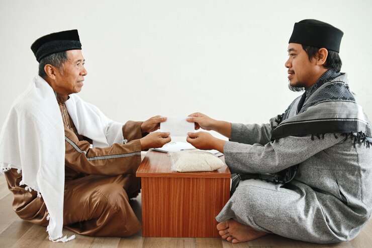 Photo young asian muslim man giving rice as food donation to senior mosque administrator for zakat fitrah