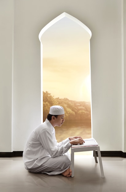 Photo young asian muslim man with cap reading holy book koran