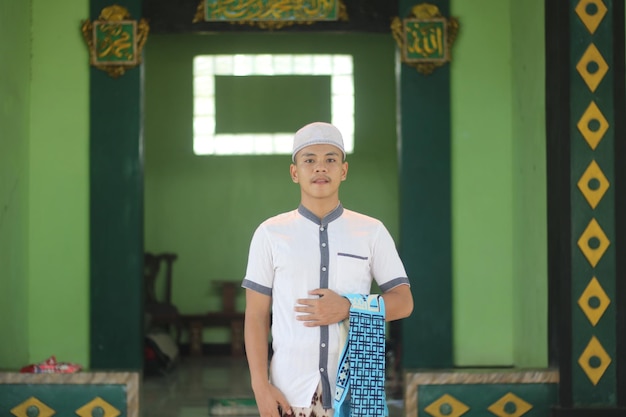 Photo young asian muslim praying in the mosque carrying a prayer mat