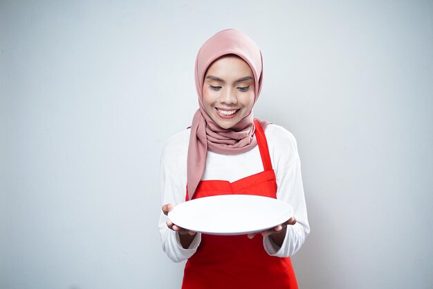 young asian muslim woman in apron standing and holding empty white plate