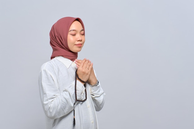 Young Asian Muslim woman praying to god with tasbih isolated over white background