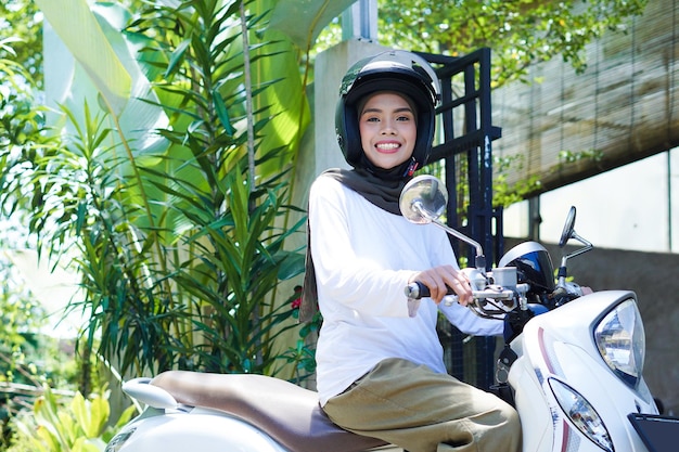 ヘルメットをかぶってオートバイに乗る若いアジアのイスラム教徒の女性