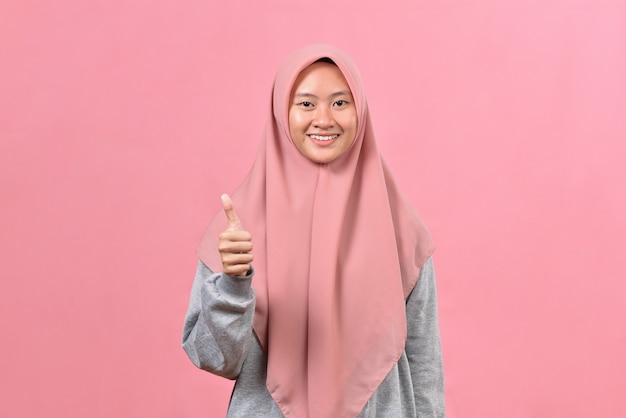 Молодая азиатская мусульманская женщина показывает палец вверх на фоне розового цвета. Копируйте пространство для копирования. Показывает большой палец вверх.