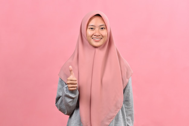 Young Asian Muslim woman showing thumb up against pink colour background. Mock up copy space. Showing thumb up.