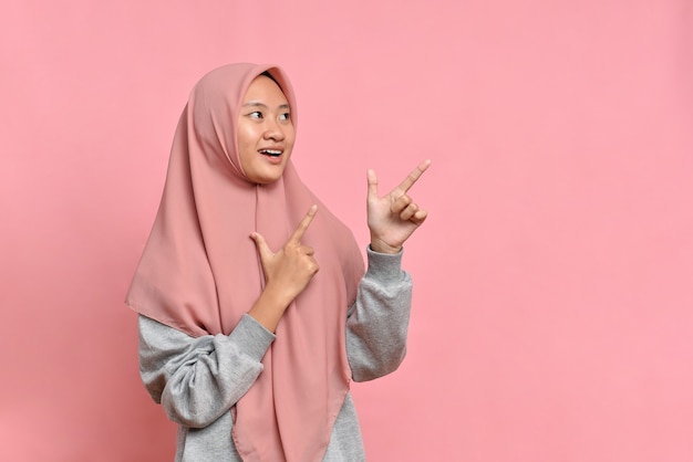 Young Asian muslim woman smiling points aside on copy space shows advertisement wears muslim casual clothes