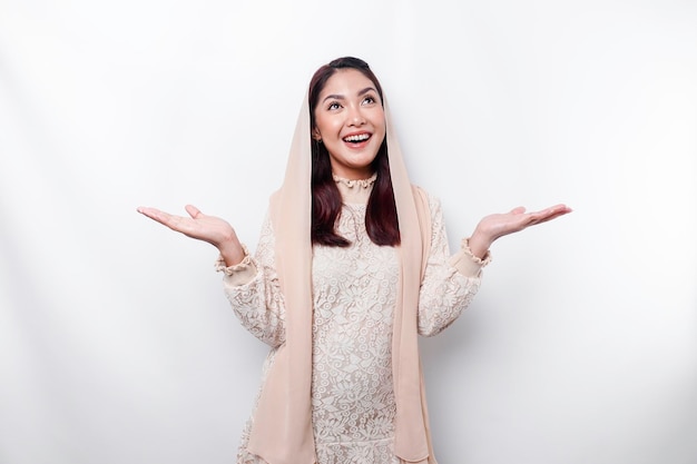 Молодая азиатская мусульманка улыбается, указывая на пространство рядом с ней