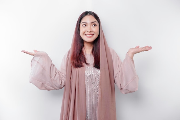 Young Asian Muslim woman smiling while pointing to copy space beside her