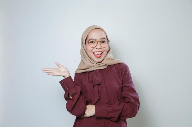 Young Asian Muslim woman wearing glasses pointing to empty space smiling feeling confident and happy