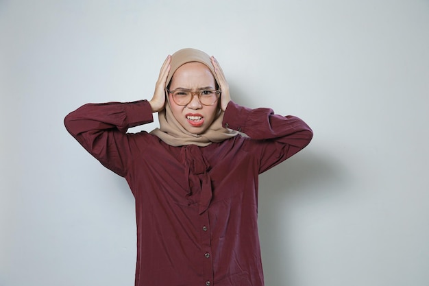 若いアジアのイスラム教徒の女性がメガネをかけて悲しい両耳を手で覆っています。