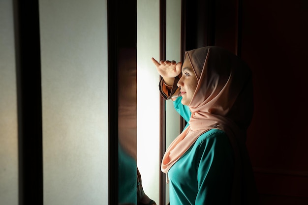 Young Asian  muslim woman wearing headscarf  front window mood light on face dark background