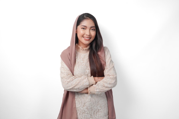 Young Asian Muslim woman wearing headscarf veil smiling to the camera with crossed arms pose full of confidence isolated by white background